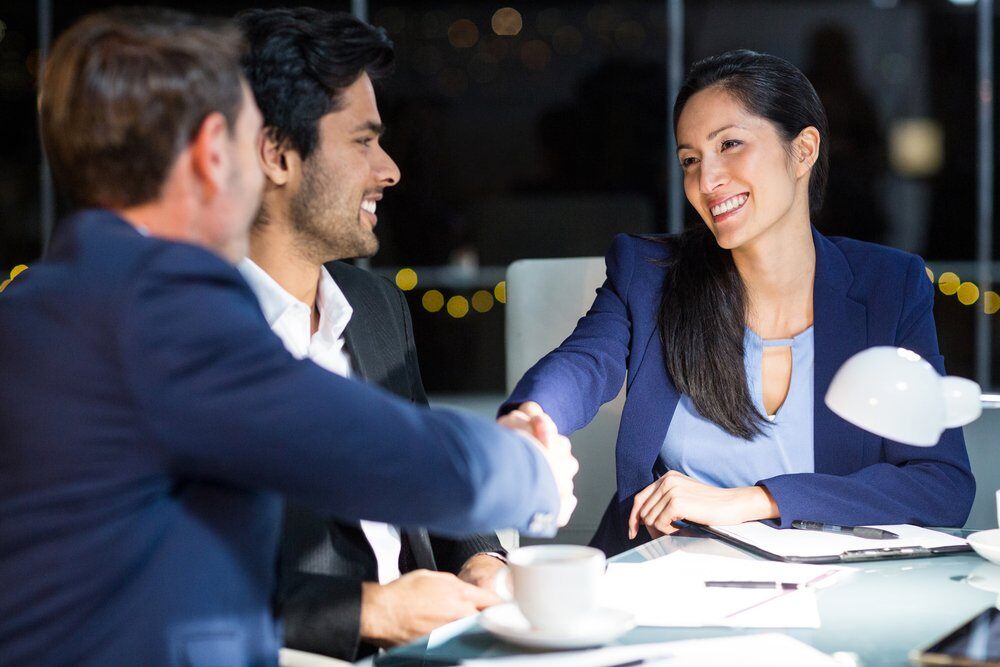 business woman and two business men shaking hands at table