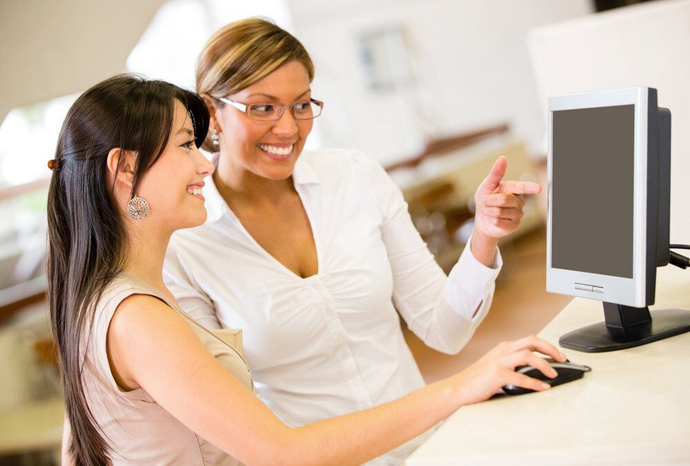 woman helping another woman find something in a computer